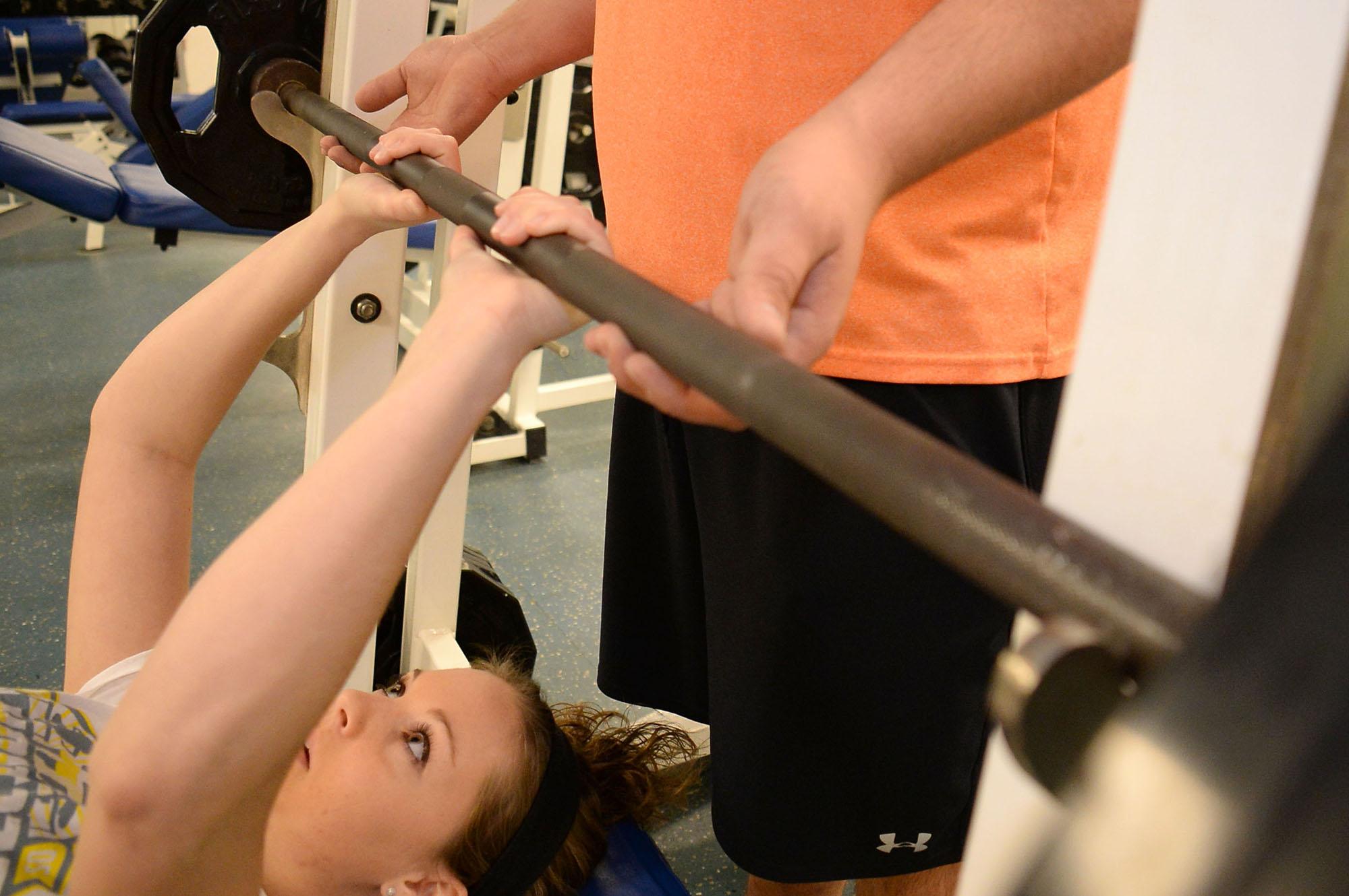 A student spotting another student while she is lifting weights